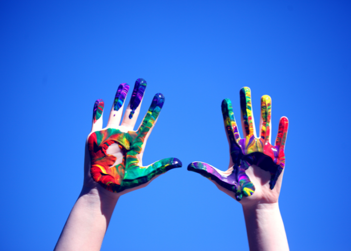 Photo of two paint covered hands against a brilliant blue sky